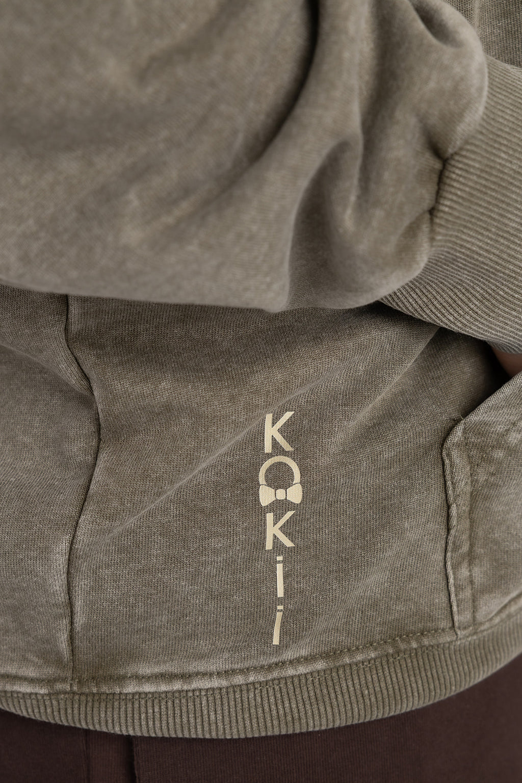 Vertical KOKii logo print near the hem of the washed olive Lucas 1:37 hoodie