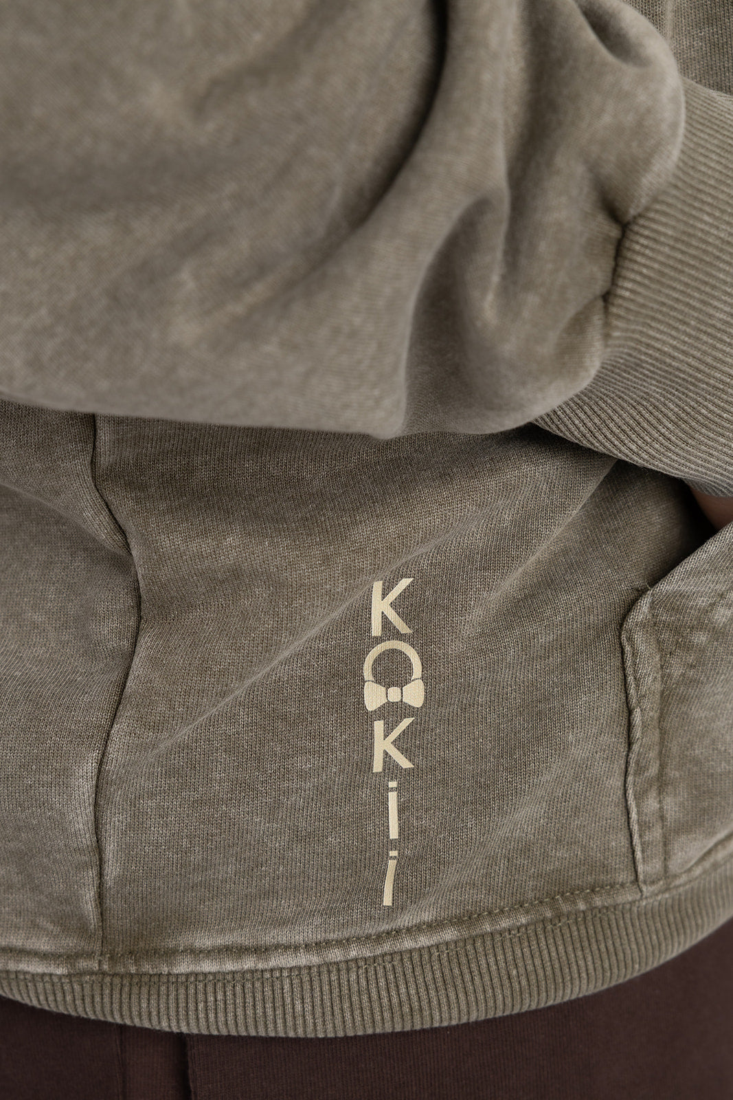 Vertical KOKii logo print near the hem of the washed olive Lucas 1:37 hoodie
