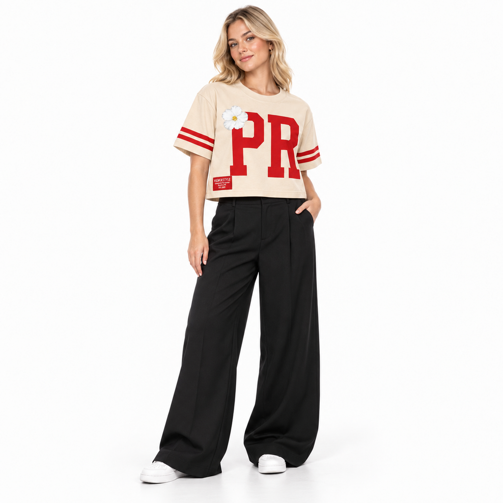 Full-length view of a model in the Kokii Style PR Varsity Stripe Flor de Maga Crop Top, beige & red, styled with black wide-leg trousers and white sneakers